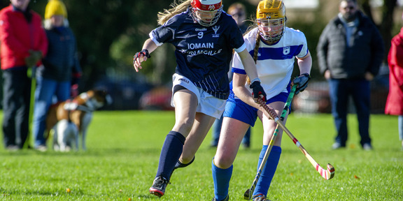 Two players playing shinty in a pitch