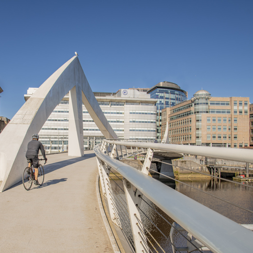 cyclist crossing the Tradeston Bridge in the sunshine, with office building in the background