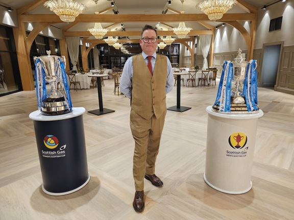 Man standing in a event room between two silver football trophies