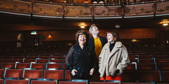 Comedians Elaine C Smith, Mark Nelson And Zara Gladman stand in a row of theatre seats.