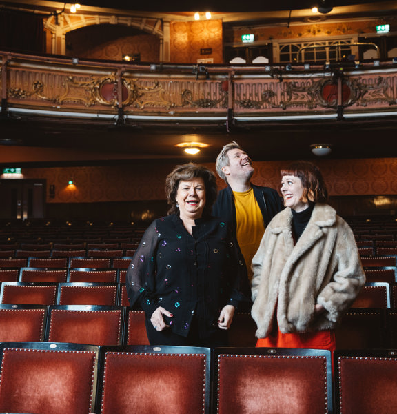 Comedians Elaine C Smith, Mark Nelson And Zara Gladman stand in a row of theatre seats.