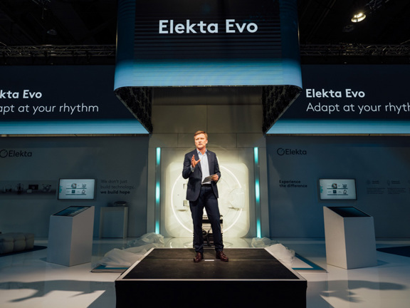 Man on a stage presenting in front of a backdrop that reads 'Elekta Evo adapt at your rhythm'