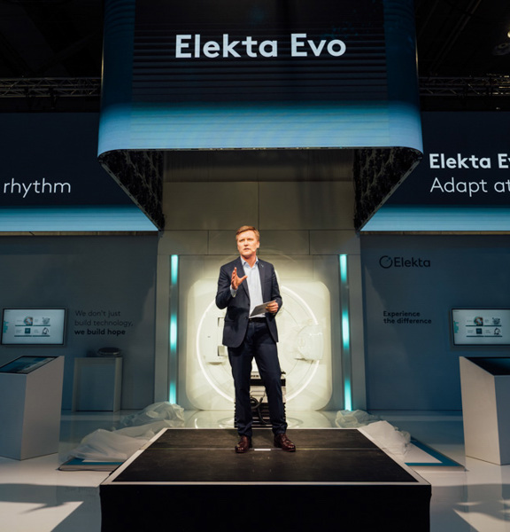 Man on a stage presenting in front of a backdrop that reads 'Elekta Evo adapt at your rhythm'