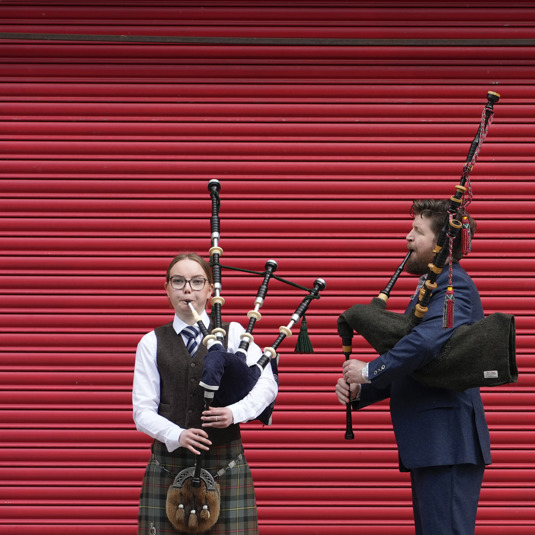 Two pipers standing infront of red shutters