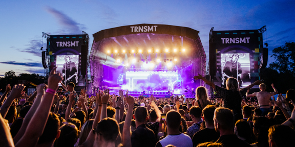 Large crowd cheers in front of TRNSMT stage, where a musician is playing guitar.