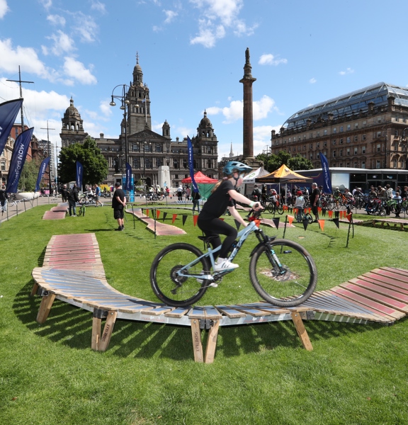 A child dressed in black rides a bike on a wooden ramp in George Square, Glasgow.