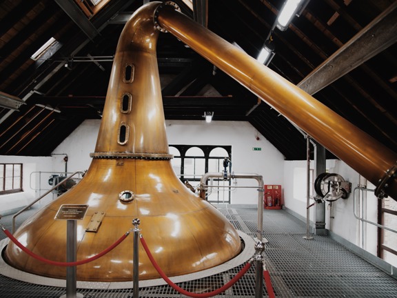 Giant copper whisky still in a white attic space with dark wooden ceiling