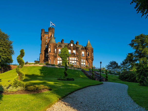 Baronial castle style building on top of a hilly landscaped garden