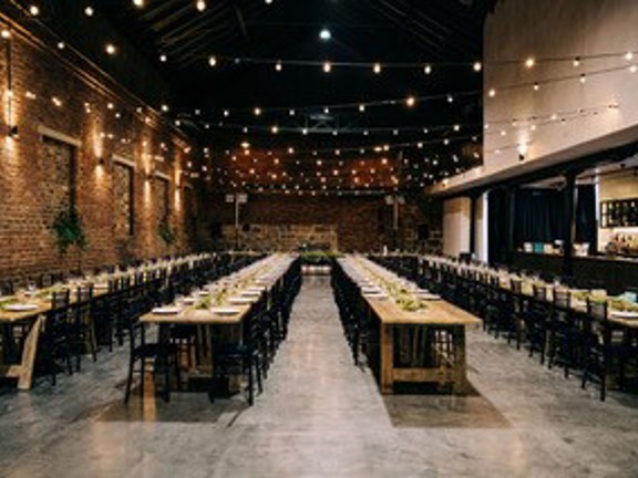 Large room set up with long trestle tables for dinning with festoon lights above