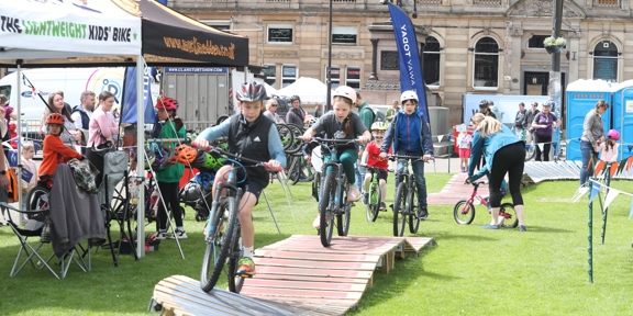 Three children cycle on a wooden ramp, in George Square, Glasgow.