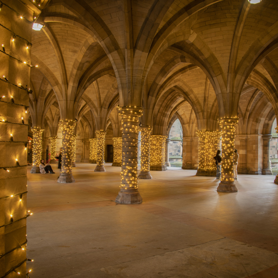 Gothic-revival-style arches and columns of University of Glasgow Cloisters, with fairy lights wrapped around each column.