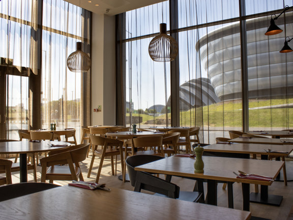 Dining area with multiple tables and chairs set as a restaurant. Floor to ceiling windows look out to the SEC and Hydro Arena in Glasgow.