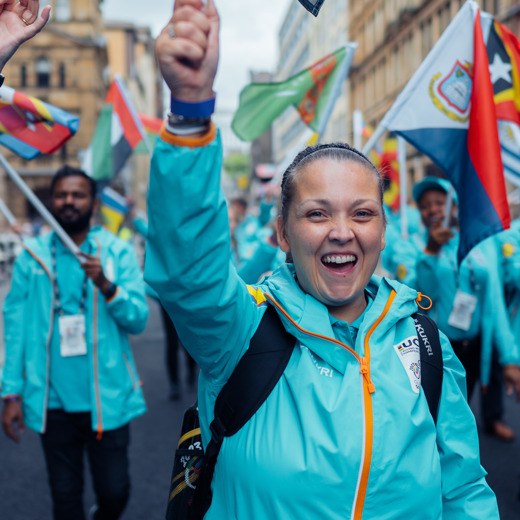 A smiling volunteer wearing a blue 2023 UCI Cycling World Championships uniform waves a flag above her head.