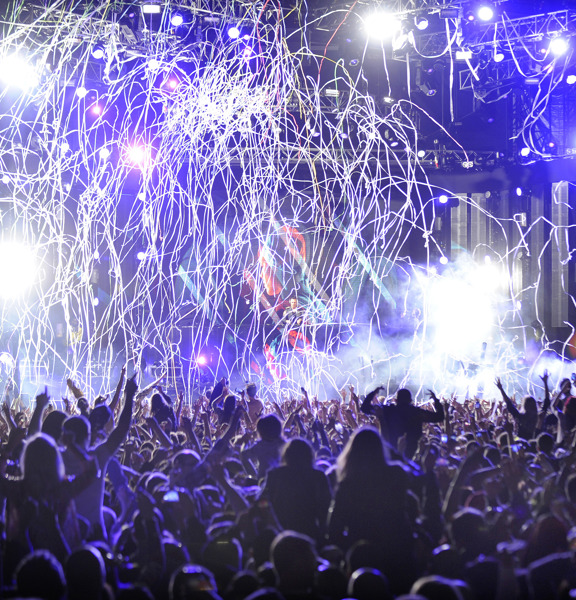 A cheering crowd is silhouetted in front of stage at Radio 1's Big Weekend Glasgow, the lights are blue and string confetti is falling from the sky.