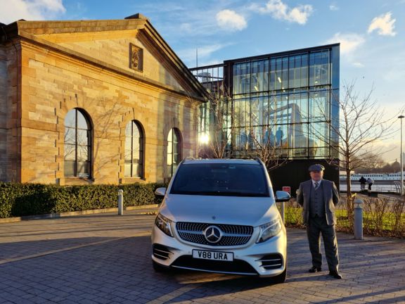 Man standing next to silver Mercedes in front of a whisky distillery