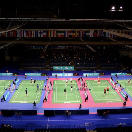 A view of five badminton courts, national flags hang from the ceiling.