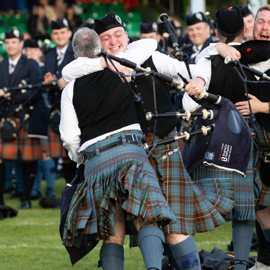 A group of pipers wearing kilts hug and celebrate their win at the World Pipe Band Championships.