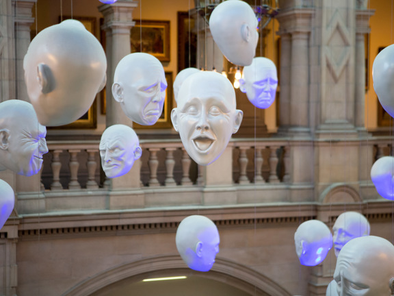art exhibit consisting of white acrylic heads with expressions of various emotions, hanging from the ceiling in the Kelvingrove Art Gallery and Museum