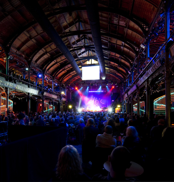 Audience watches a performance in Old Fruitmarket, Glasgow. The stage features a Celtic banner.