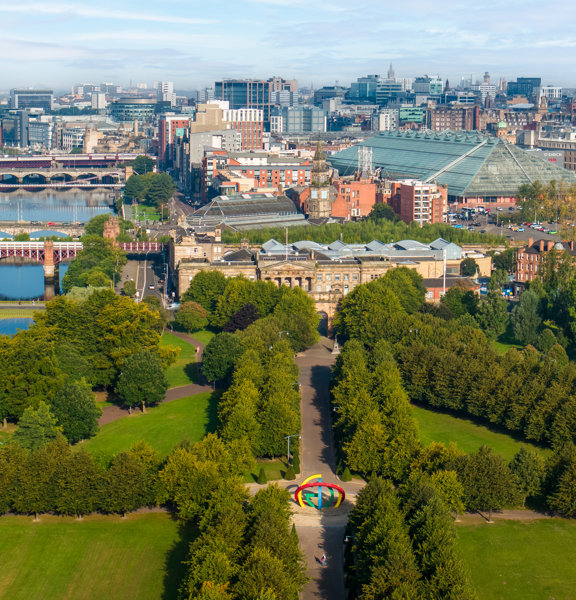 Drone shot of Glasgow Green, the River Clyde and city centre buildings on a sunny day.