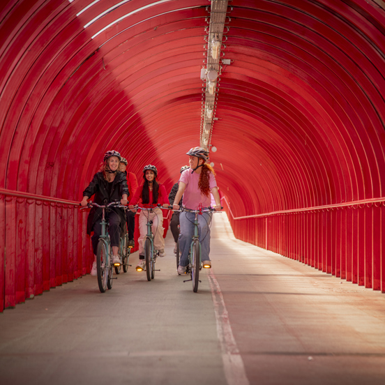 Five people cycle through covered red walkway in Glasgow.