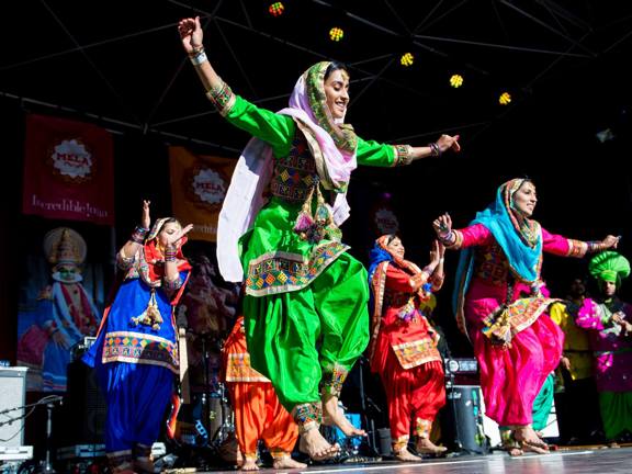 A group of women dancers in traditional clothing dance on stage in the sunshine at Glasgow Mela.