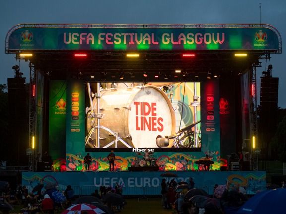 Tide Lines band performs onstage at dusk, the sign reads UEFA Festival Glasgow.