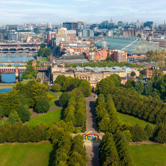 Sunny view of the tree-lined paths of Glasgow Green, on the bank of the River Clyde with several bridges and Glasgow city centre in the background