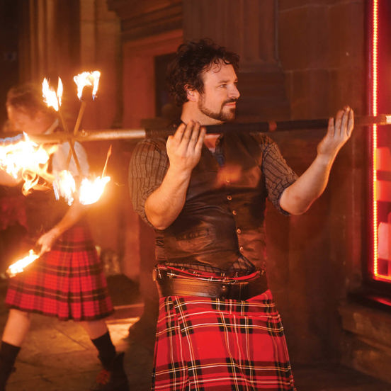 man in red kilt holding flaming 10-head fire staff