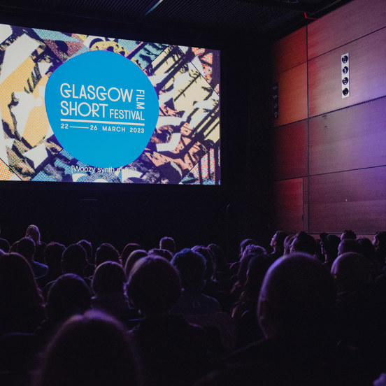 Audience facing the screen in a dark theatre, the Glasgow Short Film Festival logo is on-screen.