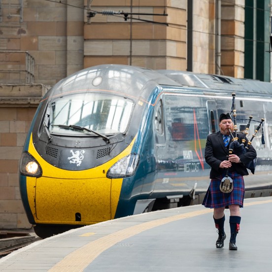 Train arrives at station with bagpiper playing on the platform and visitors arriving